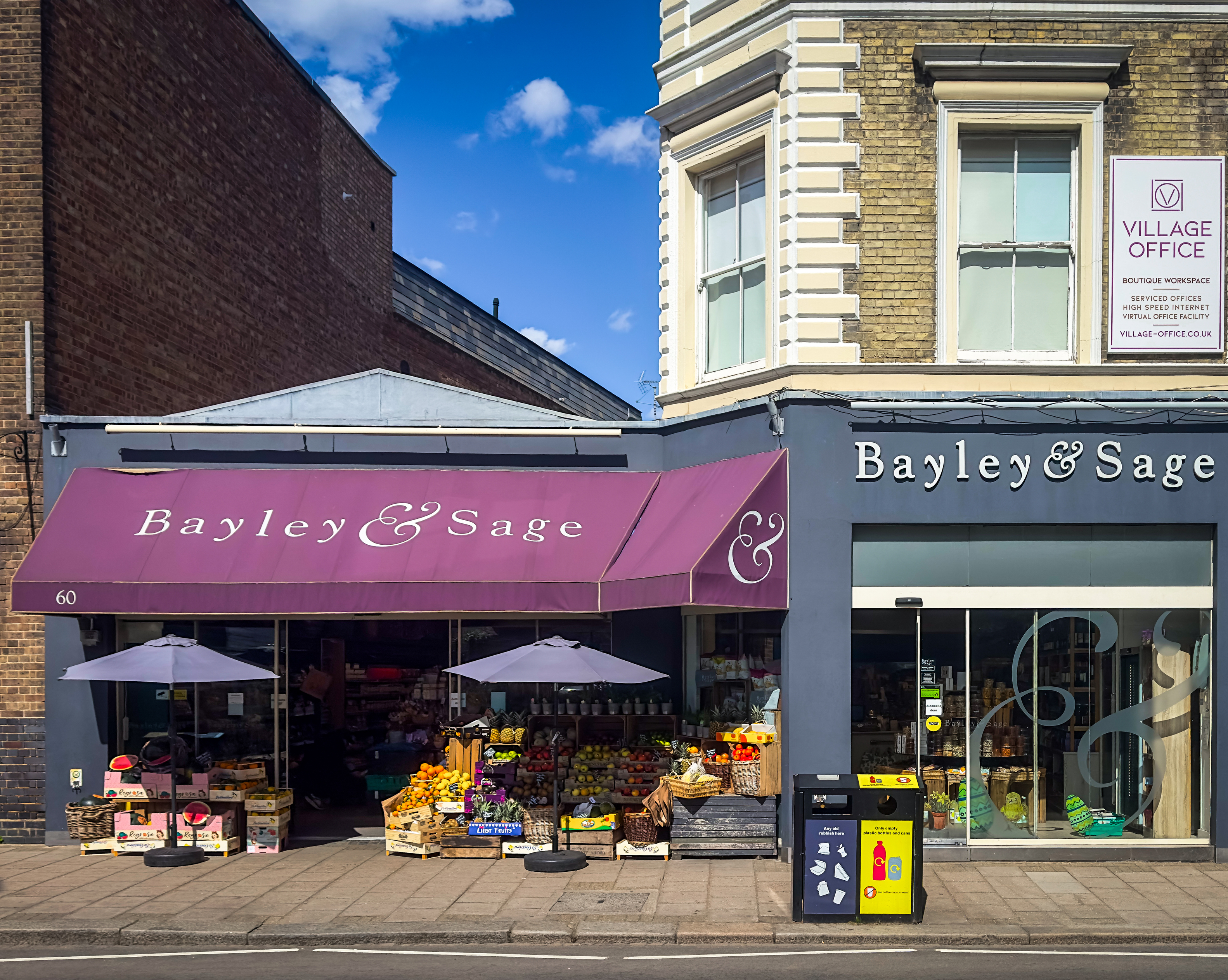 Bayley & Sage food shop in Wimbledon Village with purple awnings, fresh fruit displayed outside and the shopfront in summer light.